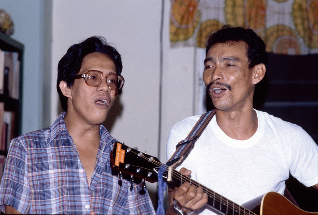 Taka with Ernie Alano, a teacher, playing the guitar in the Xavier faculty lounge, ~1975.